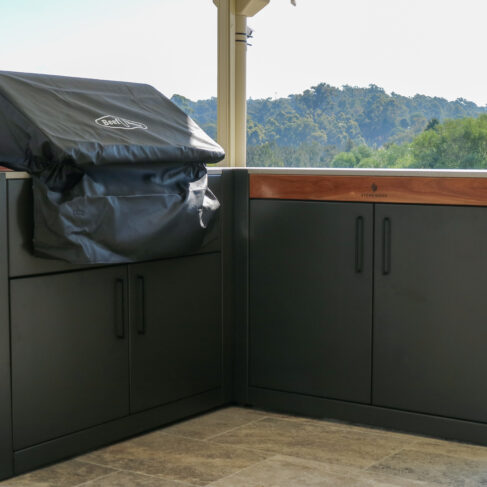 Stonewood Monument and Kreta Benchtop modular outdoor kitchen setup in Brisbane, featuring sleek black aluminum cabinets with a covered barbecue grill