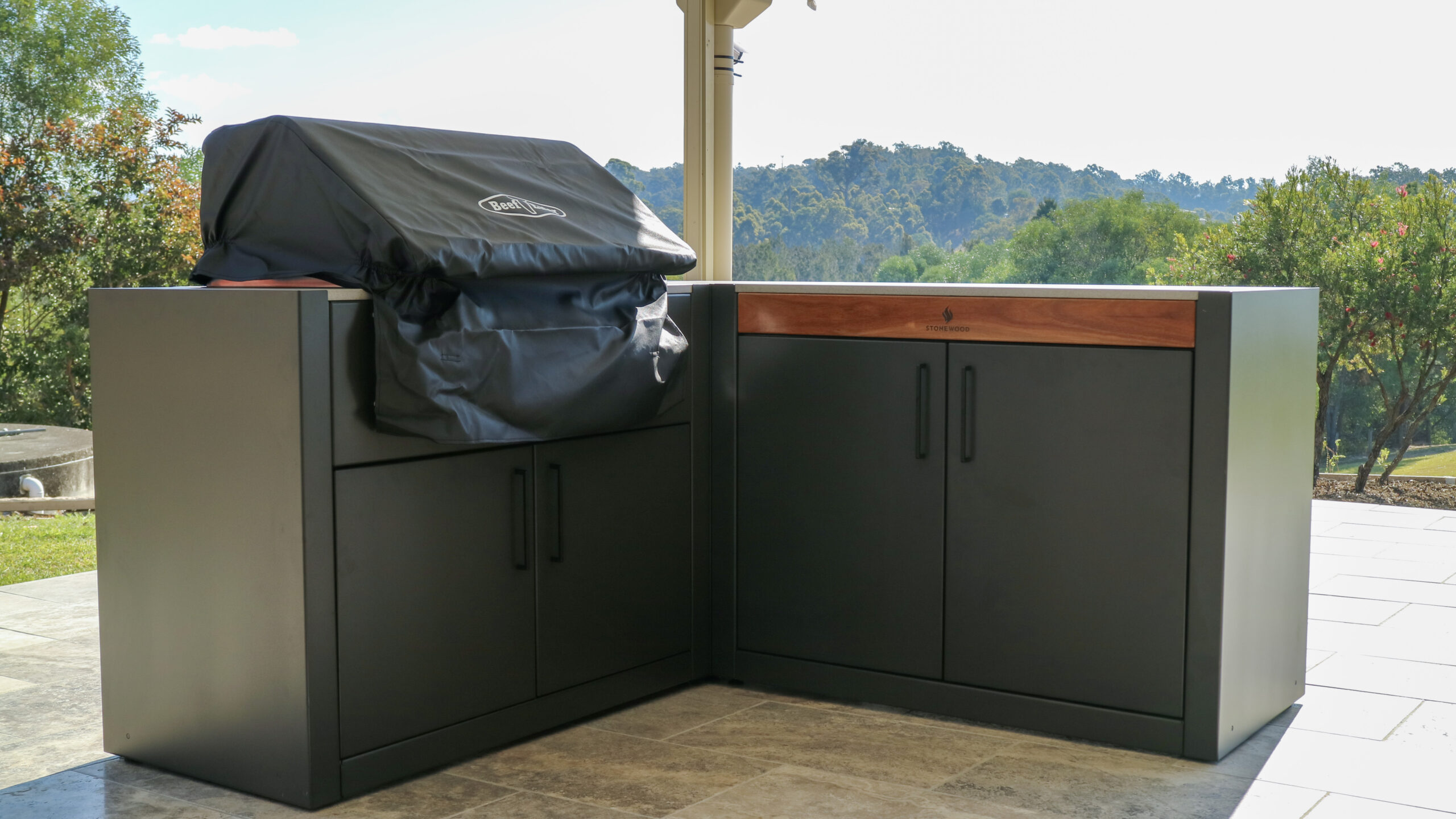 Stonewood Monument and Kreta Benchtop modular outdoor kitchen setup in Brisbane, featuring sleek black aluminum cabinets with a covered barbecue grill